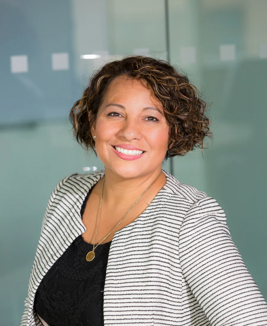 Smiling woman with curly dark hair in a striped blazer, photographed in soft natural light