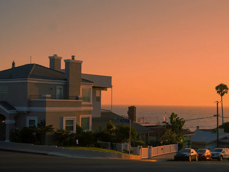 Two-story coastal home at sunset with the ocean on the horizon