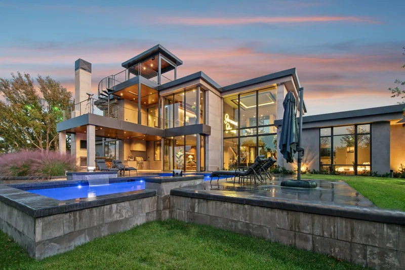 Contemporary glass-and-stone estate with a lit pool at twilight